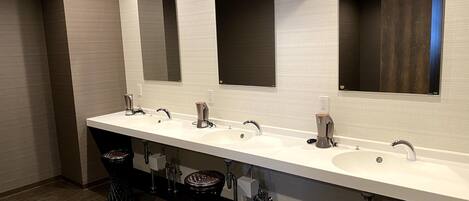 A modern bathroom with three sinks, a large mirror, and an air conditioning unit.
