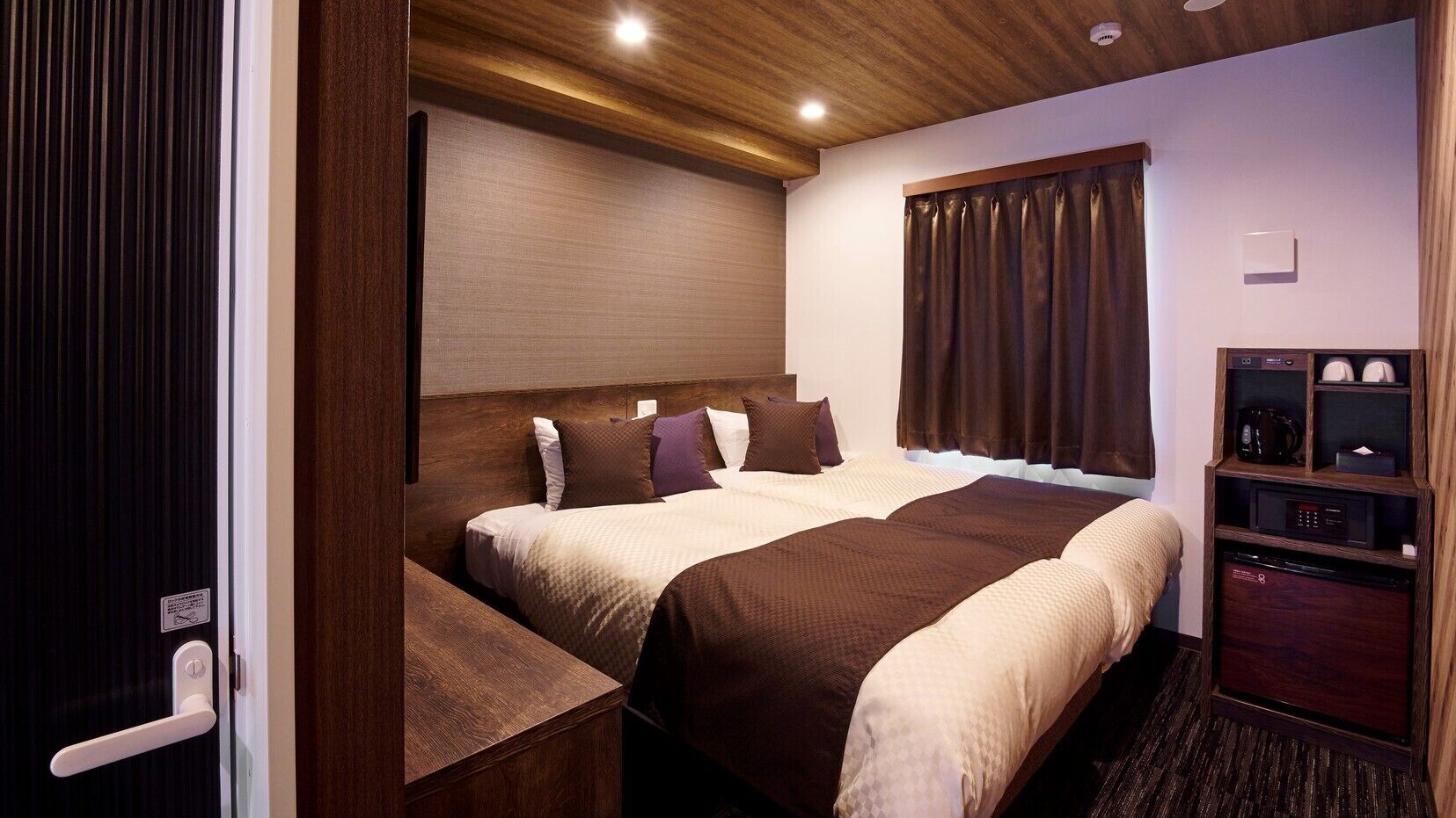 Ein Hotelzimmer mit zwei Betten, einem Holzkopfende, einem kleinen Schreibtisch, einer Mikrowelle und einem Schrank.
