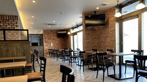Ein Restaurantinneres mit Ziegelwänden, Holztischen und -stühlen sowie einem großen Fernsehbildschirm.