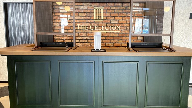 Ein Empfangsschalter mit Backsteinwand im Hintergrund, zwei Glastauschüben und einem Schild mit der Aufschrift 'THE CLECTION'.