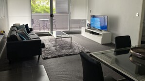 Uma sala de estar moderna com sofá, TV e mesa de centro de vidro.