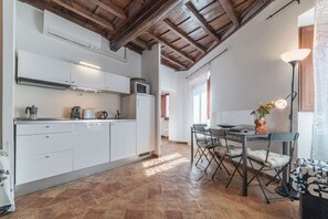 A modern kitchen with white cabinets, a dining area with a table and chairs, and a wooden ceiling.