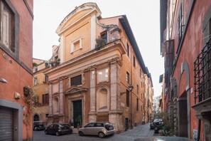 A narrow street with historic buildings, a cobblestone road, and parked cars.