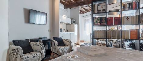 A hotel room with a large bed, two bedside tables, a TV, a bookshelf, and a kitchen area.