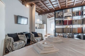 A hotel room with a large bed, two bedside tables, a TV, a bookshelf, and a kitchen area.