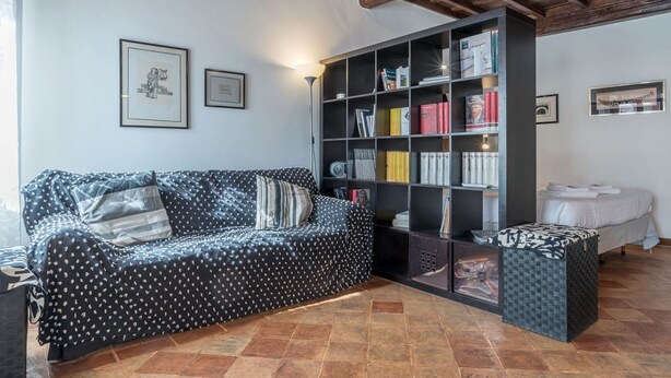 A cozy living room with a patterned sofa, a bookshelf, and a small table. - Studio close by Piazza Navona - A/C - Wi-Fi - Washer (Roma)