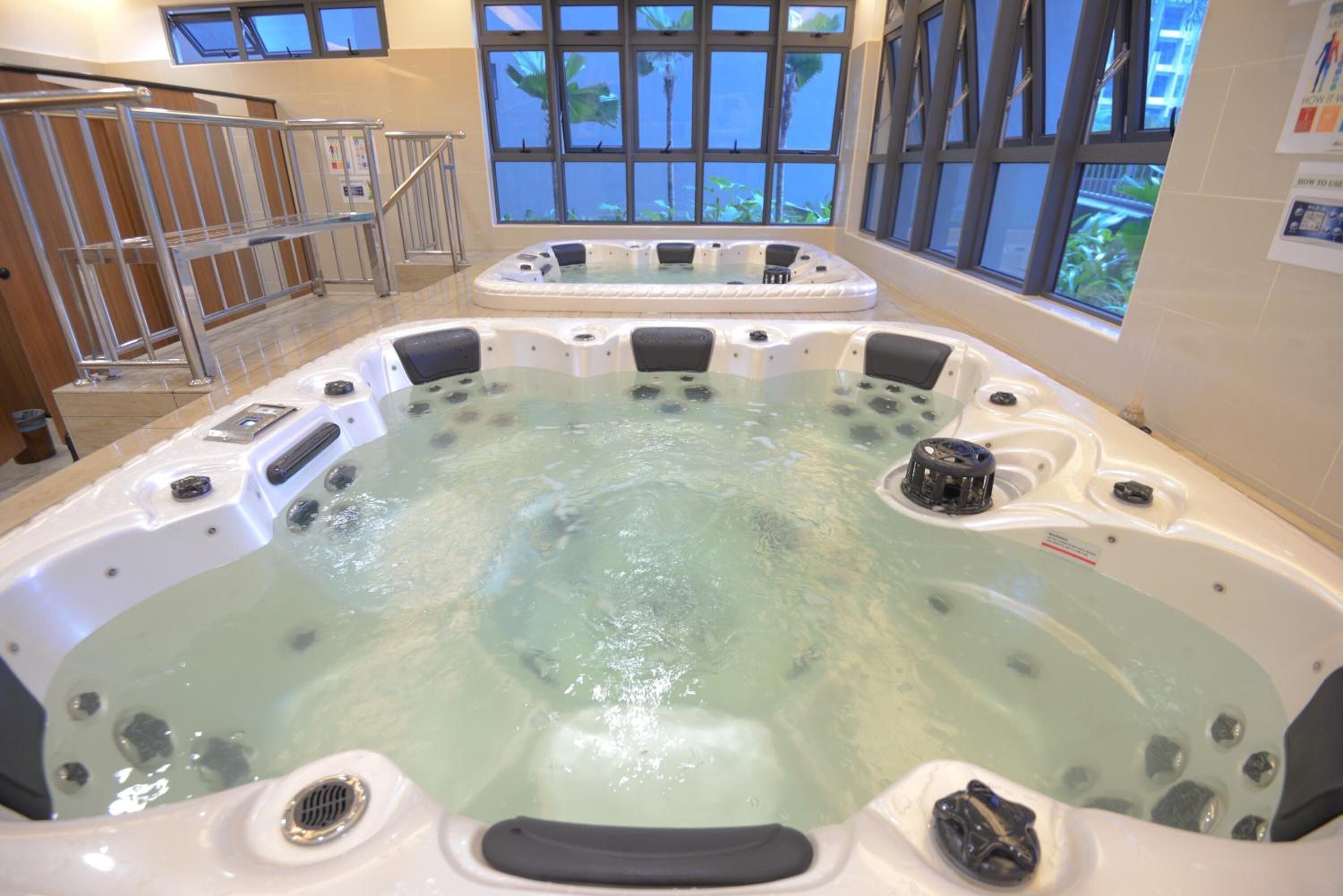 A hot tub area with multiple tubs, a metal railing, and large windows with a view of greenery.