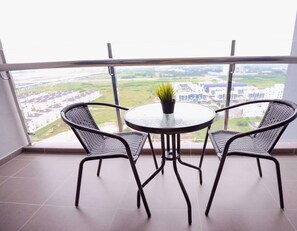 Un balcon avec deux fauteuils en osier et une petite table ronde sur laquelle est posée une plante en pot.
