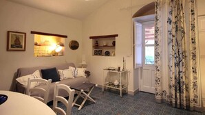 Un soggiorno accogliente con un divano, poltrone, un tavolino e una lampada decorativa. Si vede una finestra con tende e una porta che dà sull'esterno.