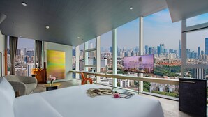 Een hotelkamer met een groot bed, een televisie en uitzicht over de stad.