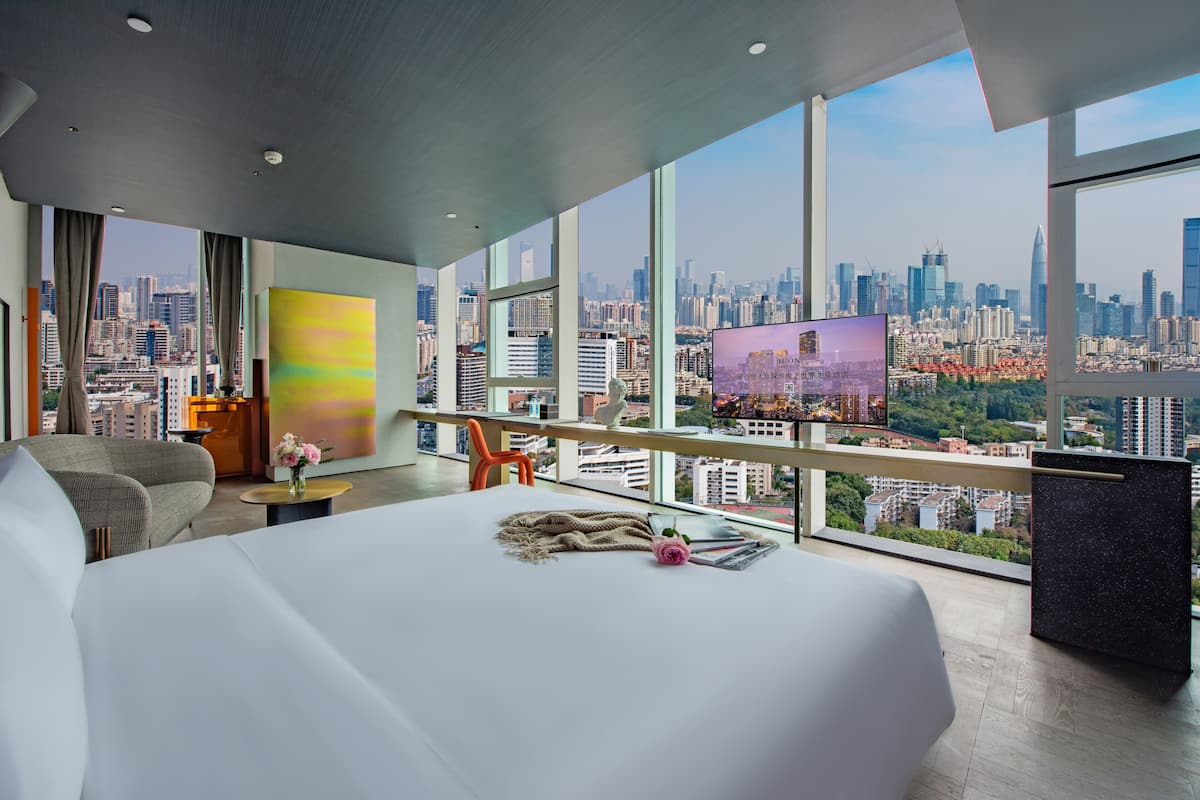 Habitación de hotel con una cama grande, televisión y vista a la ciudad.