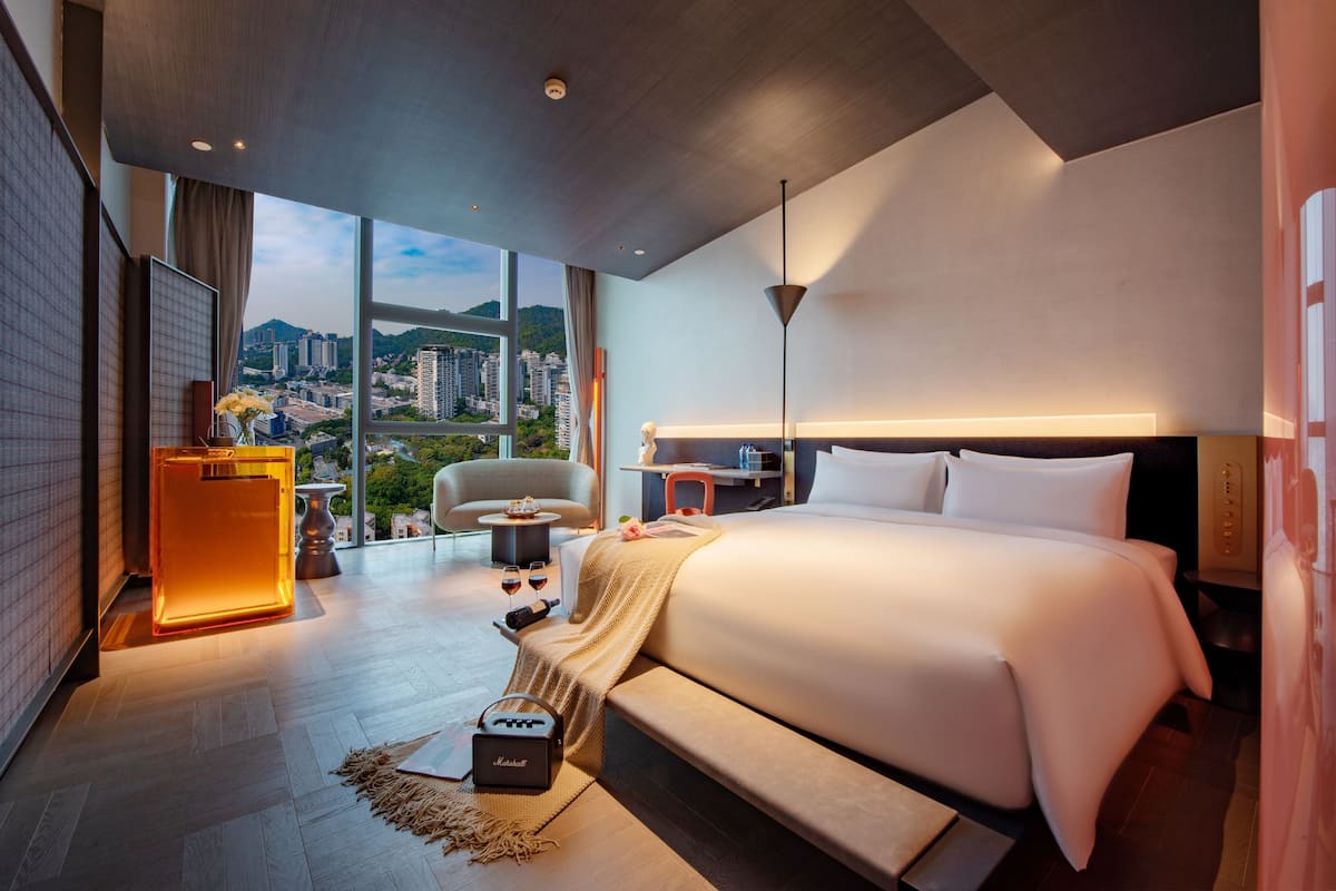 Habitación de hotel moderna con una cama grande, un escritorio, una silla y vistas a la ciudad.