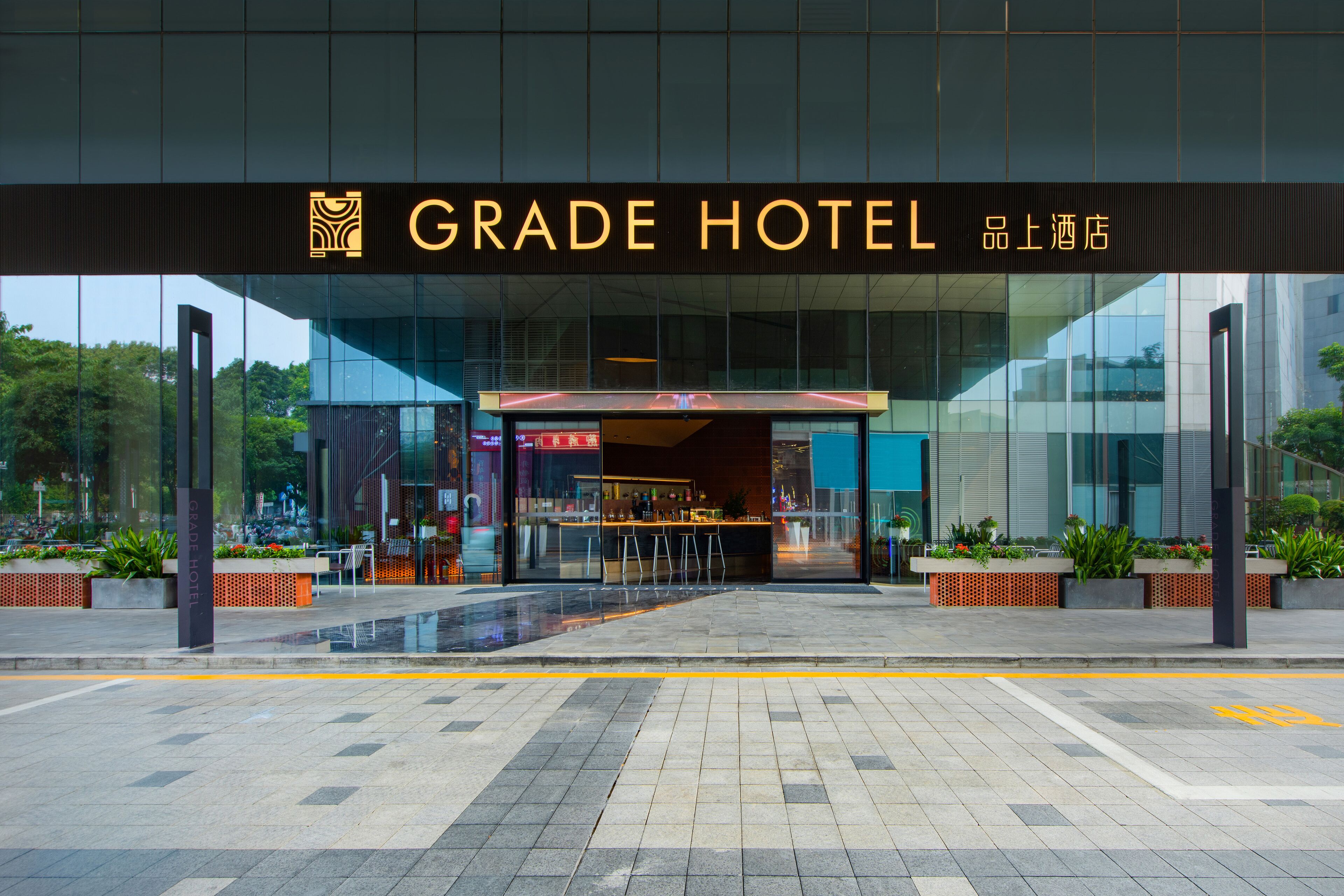 Exterior de un hotel moderno con fachada de vidrio, entrada destacada y zona de estar al aire libre.