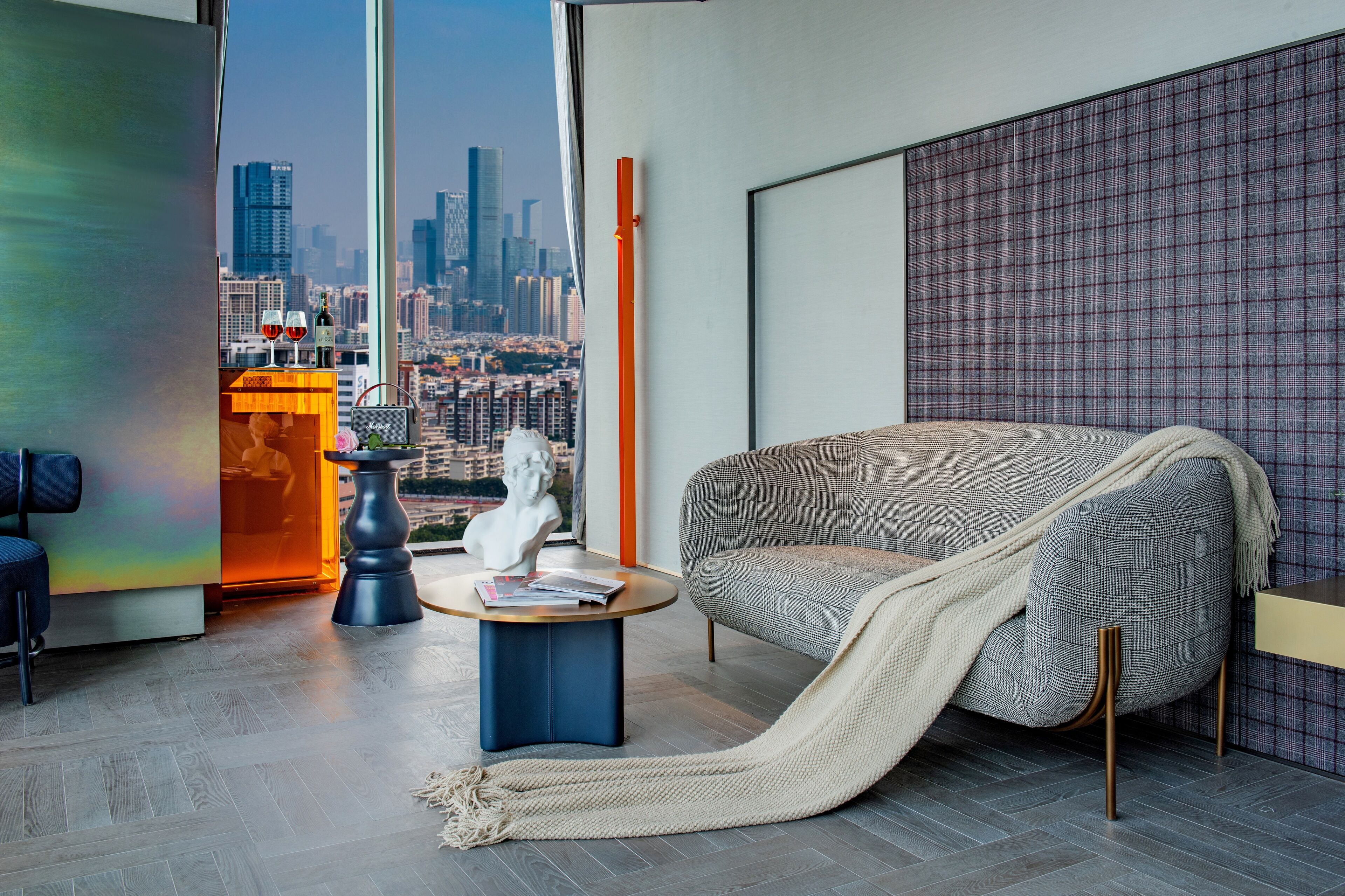 A modern living room with a city view, a sofa, a coffee table, and a statue.