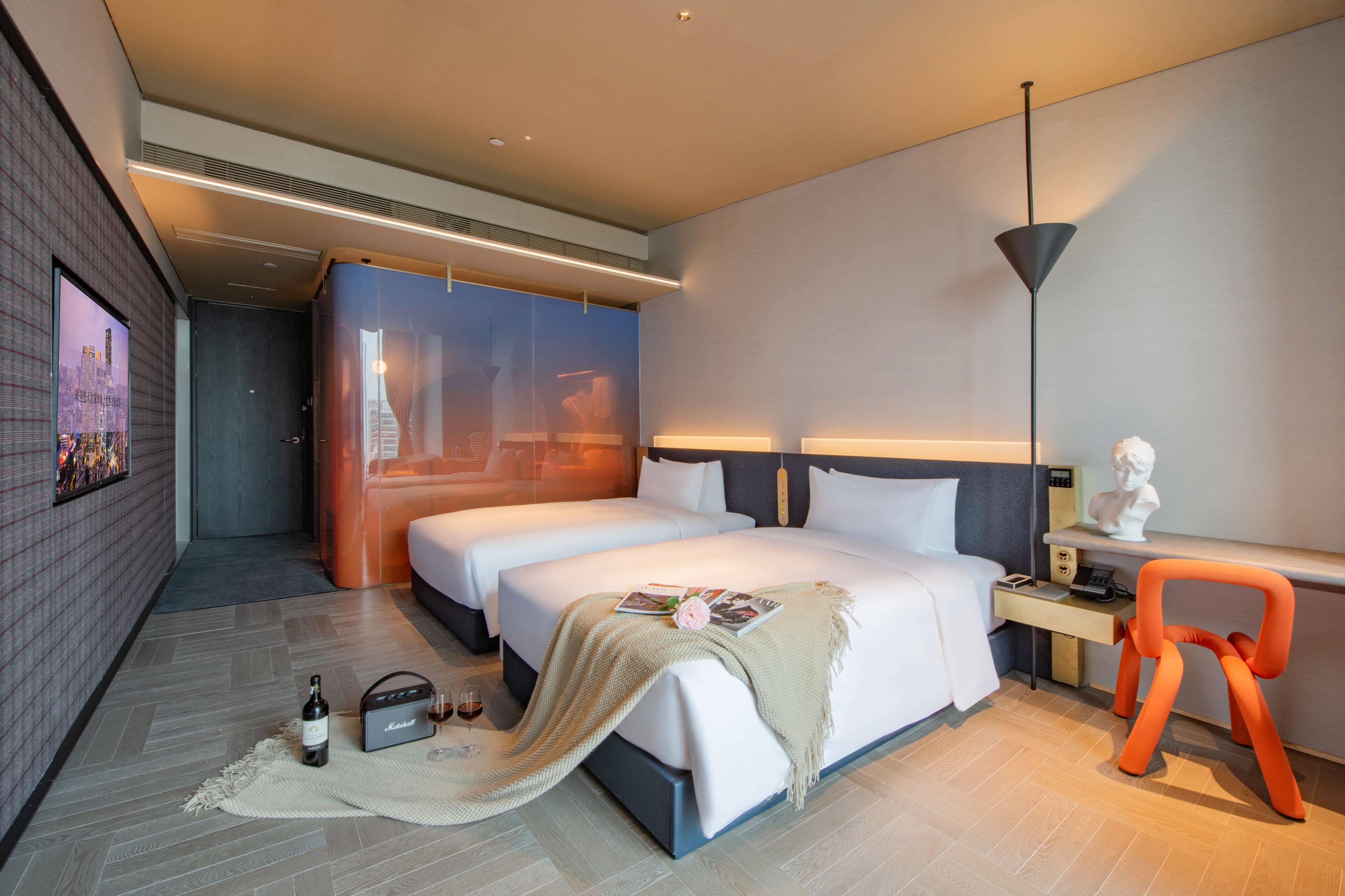 A modern hotel room with two beds, a desk, a chair, a lamp, and a large window.