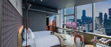 A modern hotel room with a large bed, a desk, and a view of the city skyline.