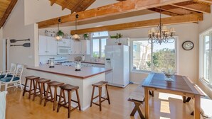 Een ruime keuken met houten balken, een centraal kookeiland met krukken, witte kastjes en een groot raam dat voor natuurlijk licht zorgt.