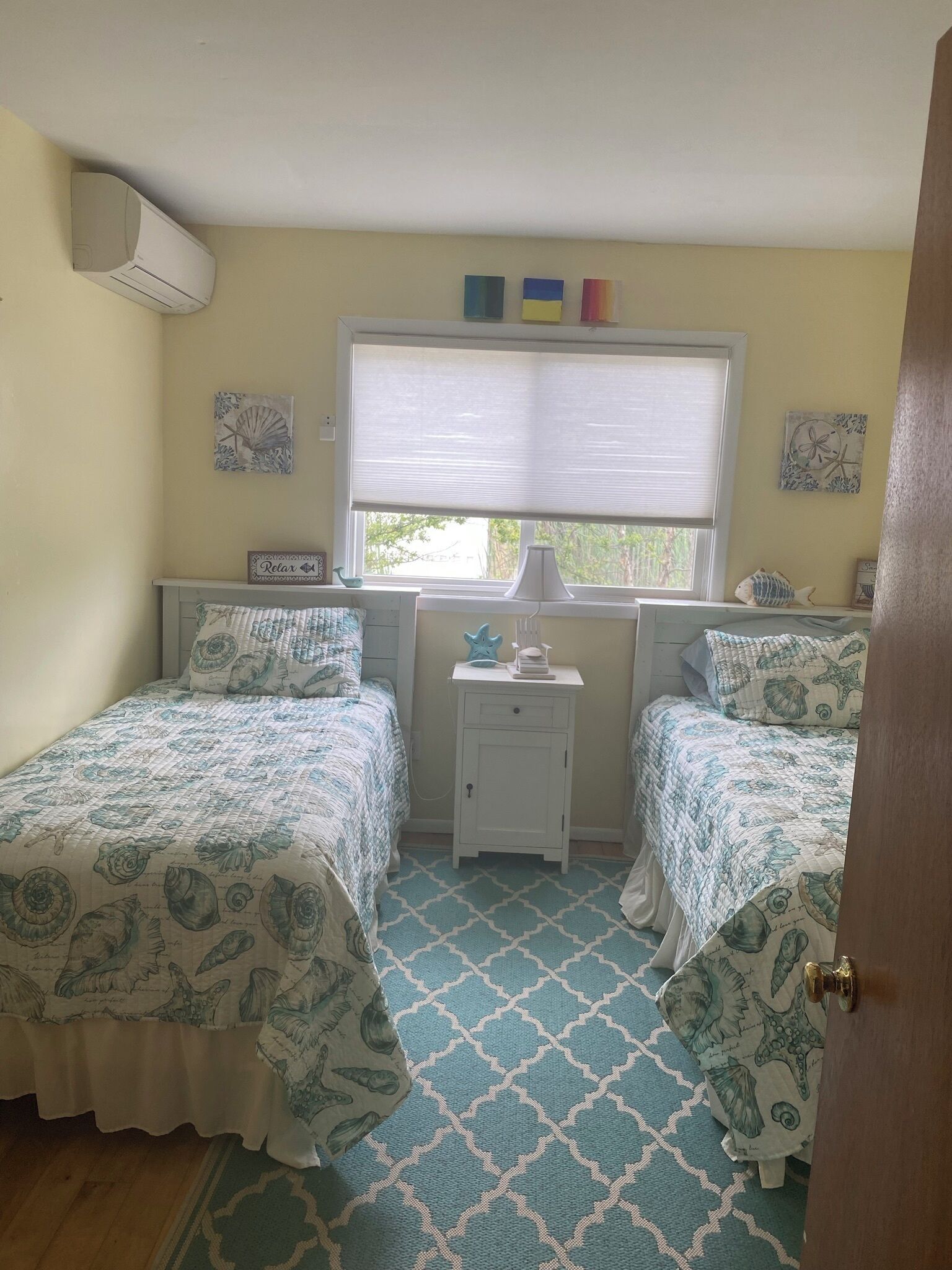 Une chambre avec deux lits, une fenêtre avec des stores, une petite table de chevet et un tapis à motifs.