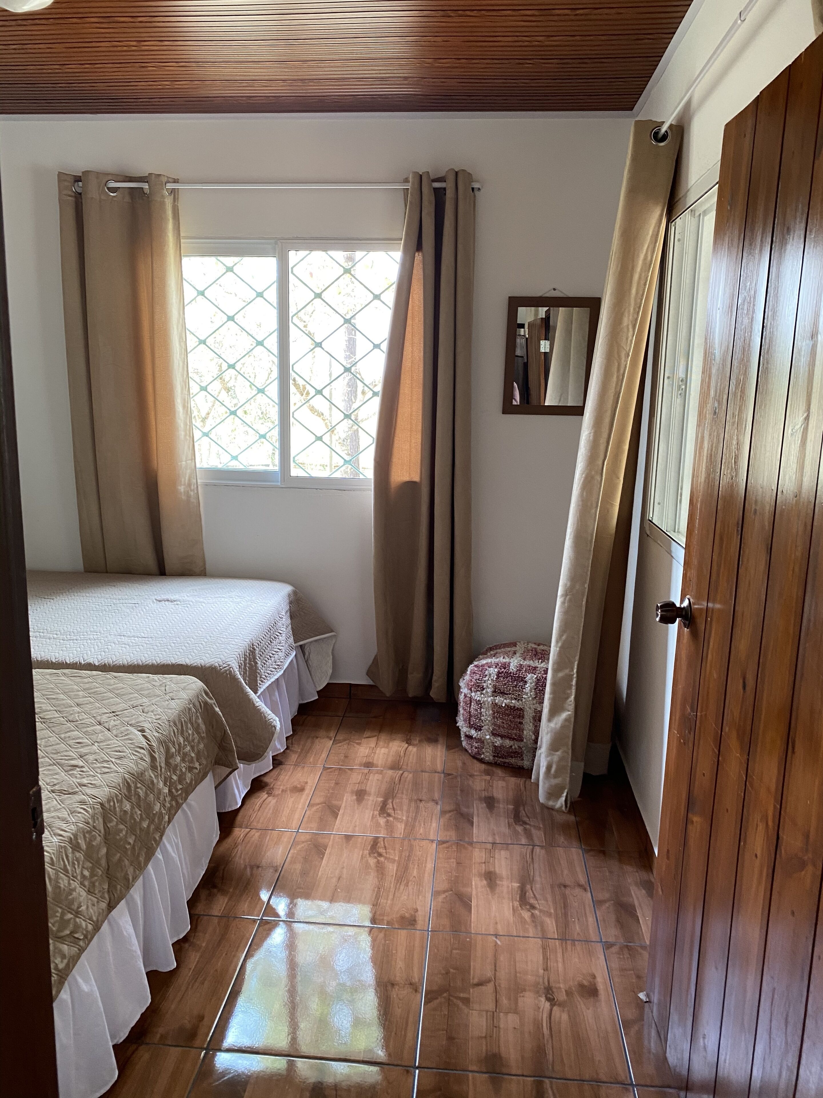 Un dormitorio con dos camas, una ventana con cortinas, un armario de madera y suelo de baldosas.