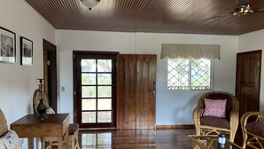 Una habitación amplia con suelo de madera, puerta de madera, muebles de mimbre y una pequeña mesa.
