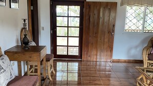 Una habitación amplia con piso de madera, una mesa de comedor con sillas, una gran puerta de madera y una ventana con vistas a la vegetación.