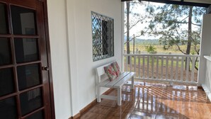 Una habitación con puerta de madera, un banco, baranda blanca y vista a árboles y colinas.