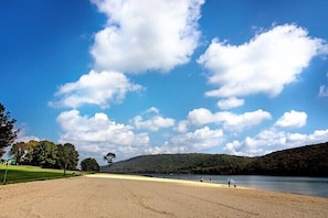 Ein Strand mit blauem Himmel, Bäumen und einer hügeligen Landschaft im Hintergrund.