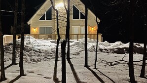 Une maison avec une cheminée en pierre, une terrasse en bois et de la neige au sol.