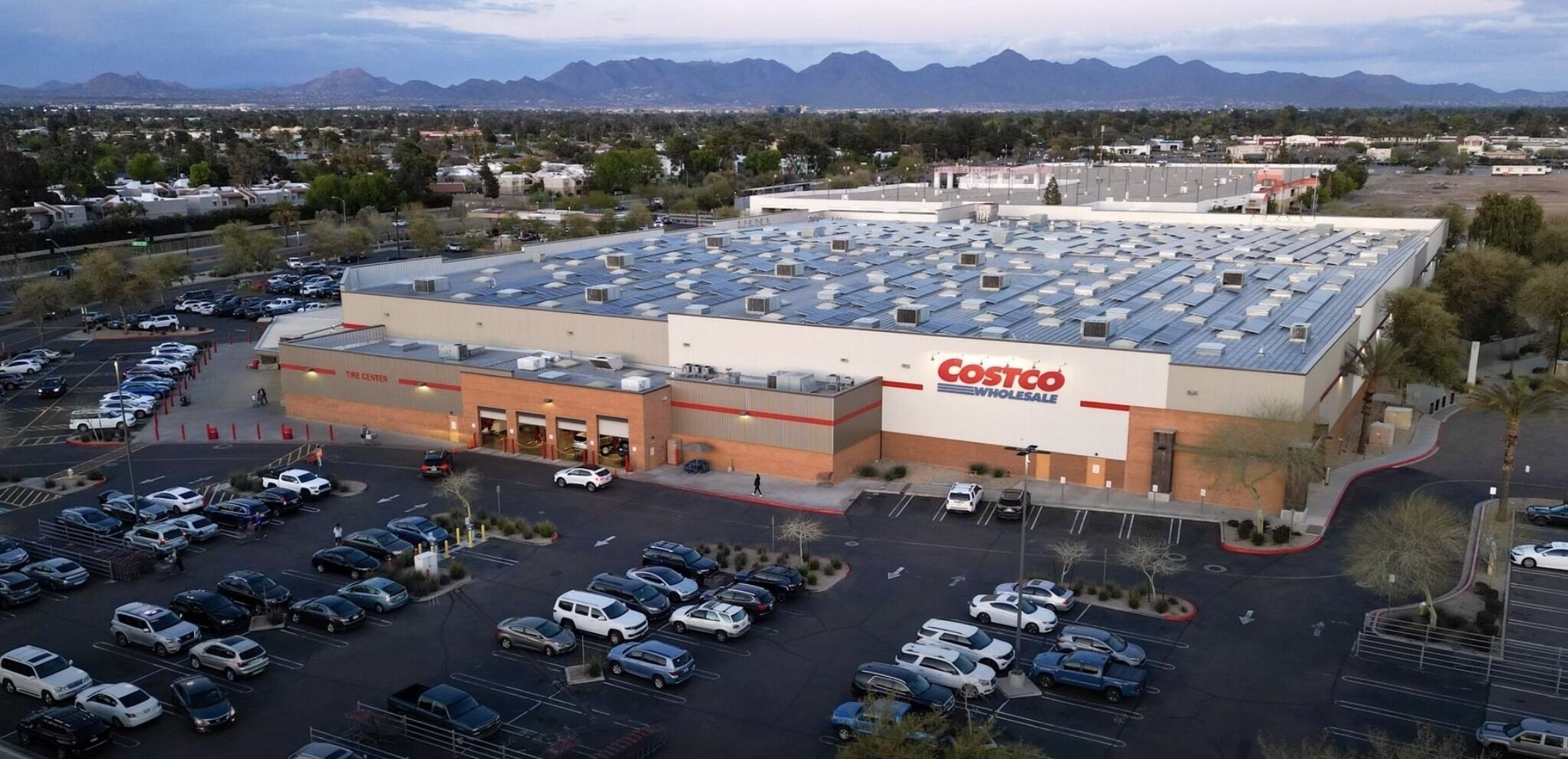 A Costco Wholesale store with a large parking lot and a mountainous backdrop.