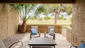 A covered patio with a table and two chairs, a large palm tree, and a view of a grassy area with trees. - Paradise Valley Paradise/ Ground Unit (Phoenix)