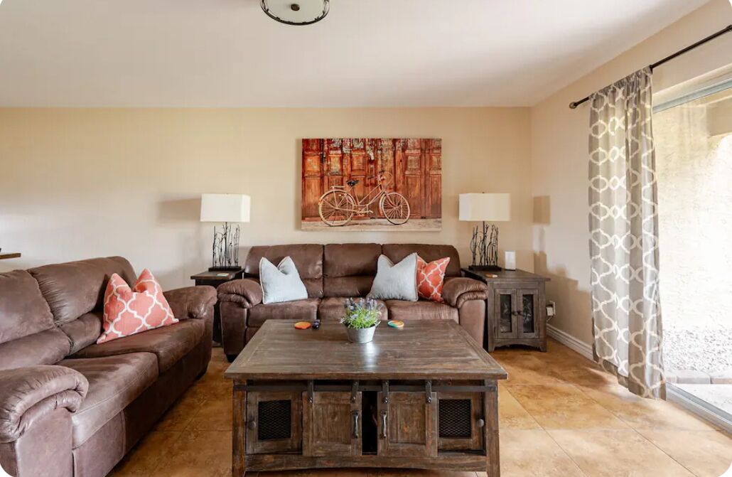 A living room with a brown leather sofa, a wooden coffee table with a plant, and a painting of a bicycle on the wall.