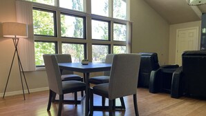 A dining area with a table and four chairs, large windows with a view of trees, a floor lamp, and a door. - Year round mountain retreat (Flagstaff)