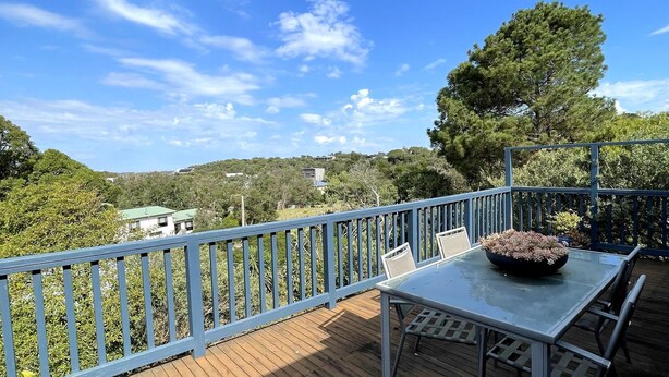 Una terraza con una mesa y sillas, con vistas a una zona boscosa y casas al fondo.