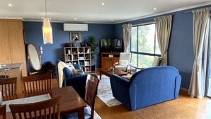 Una sala de estar con sofá, mesa de centro, televisor, estantería y comedor con sillas y mesa.