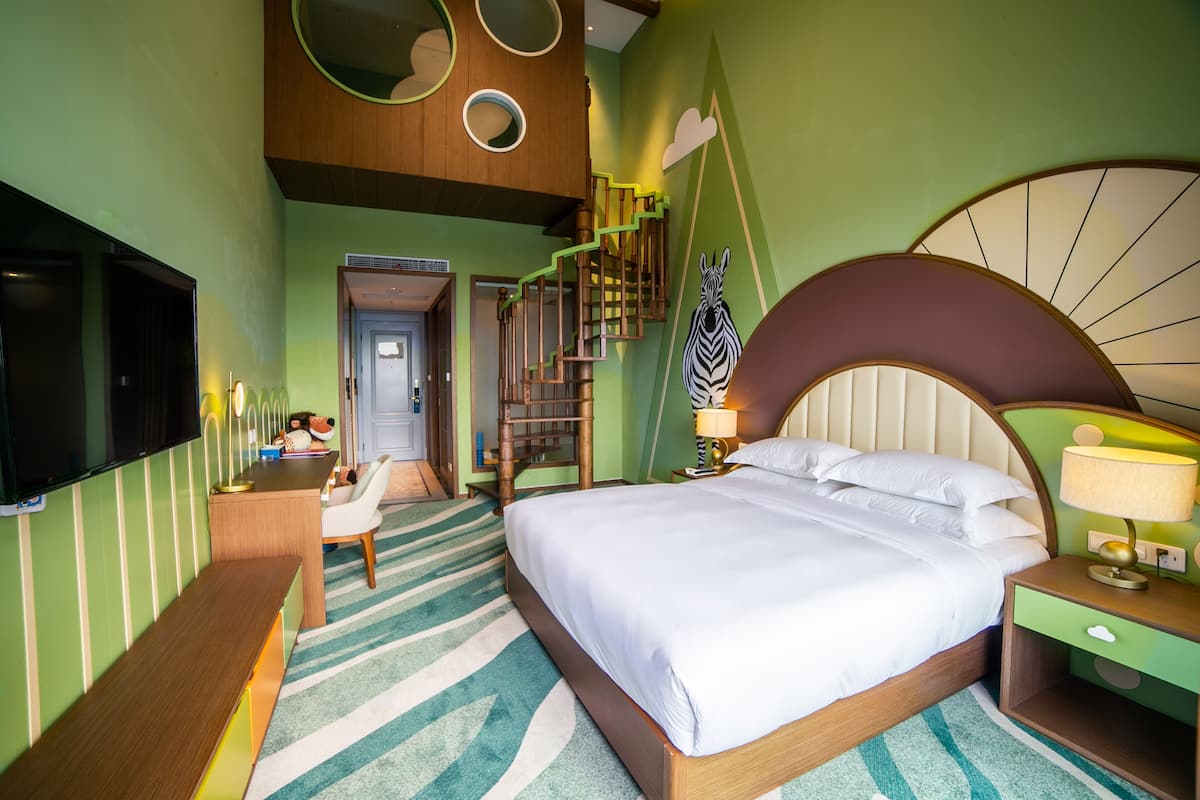 A hotel room with a large bed, a desk, a chair, a TV, a staircase, and a zebra decoration.