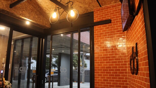 An entrance with glass doors, a brick wall, and a ceiling with exposed beams. - Double D Hotel (Pak Kret)