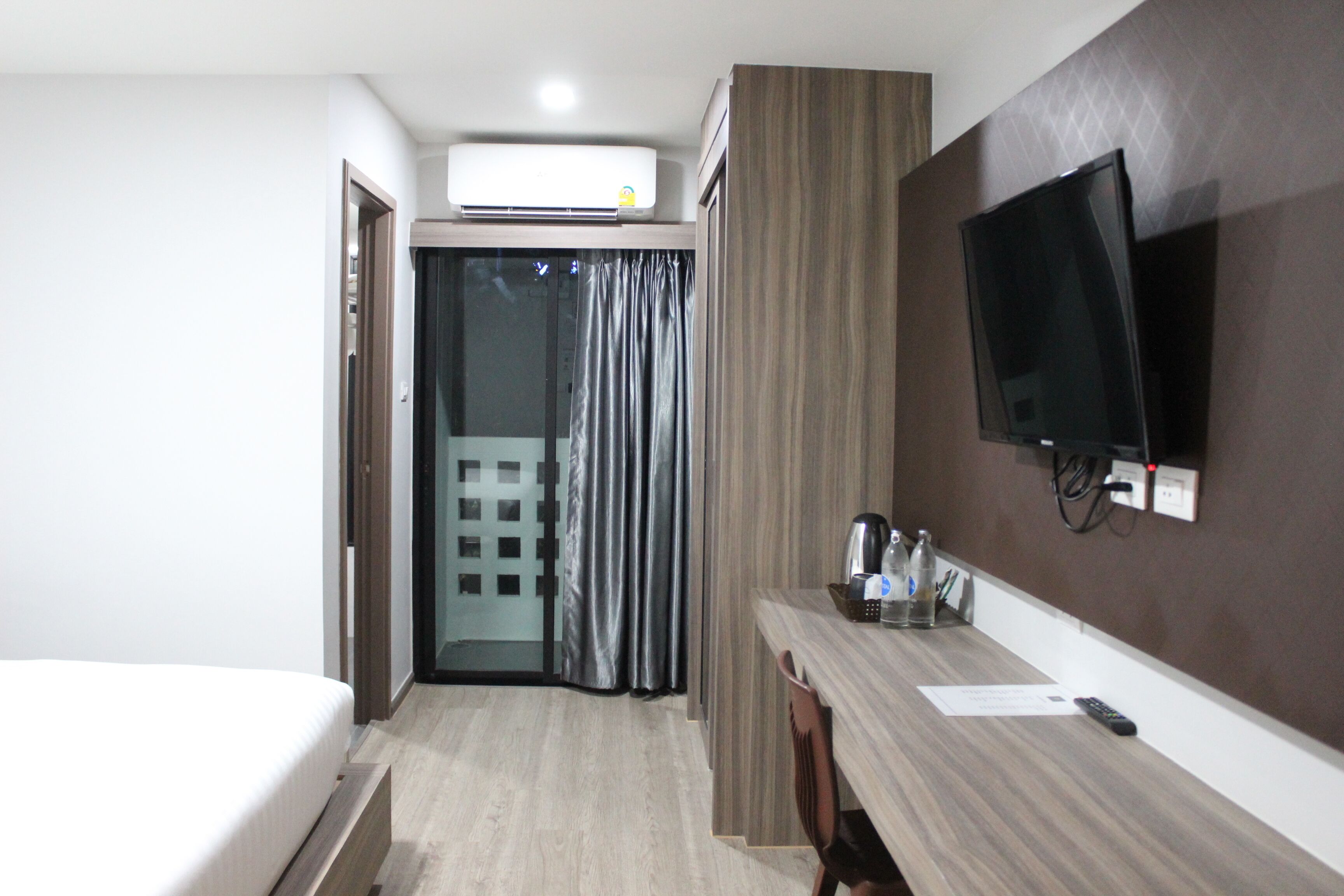 A hotel room with a bed, a desk with a flat-screen TV, a coffee maker, and a sliding door leading to a balcony.