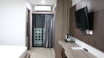A hotel room with a bed, a desk with a flat-screen TV, a coffee maker, and a sliding door leading to a balcony.
