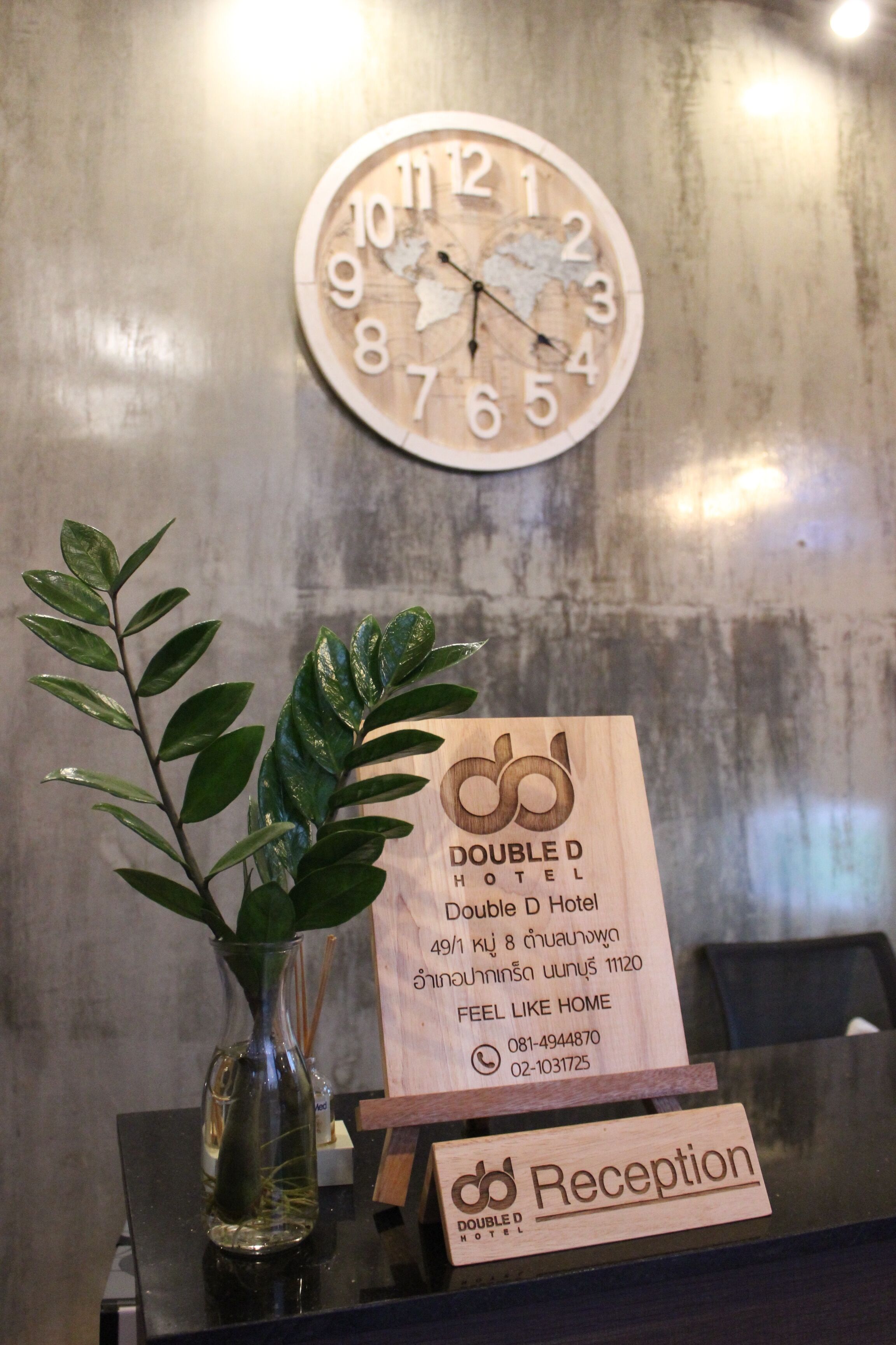 A reception desk with a clock, a wooden signboard, and a plant.