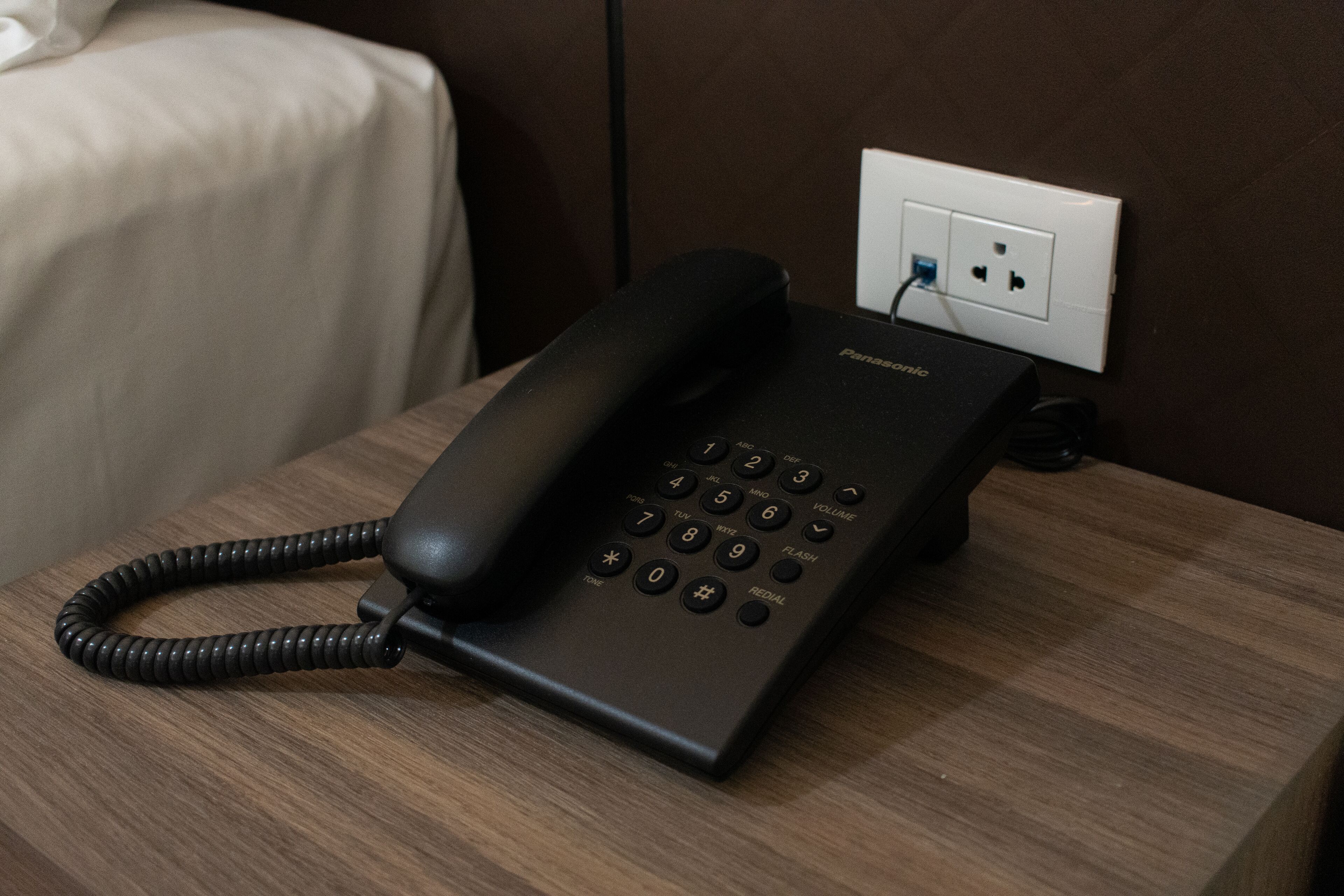 Un téléphone noir est posé sur une table en bois, à côté d’une prise électrique blanche.