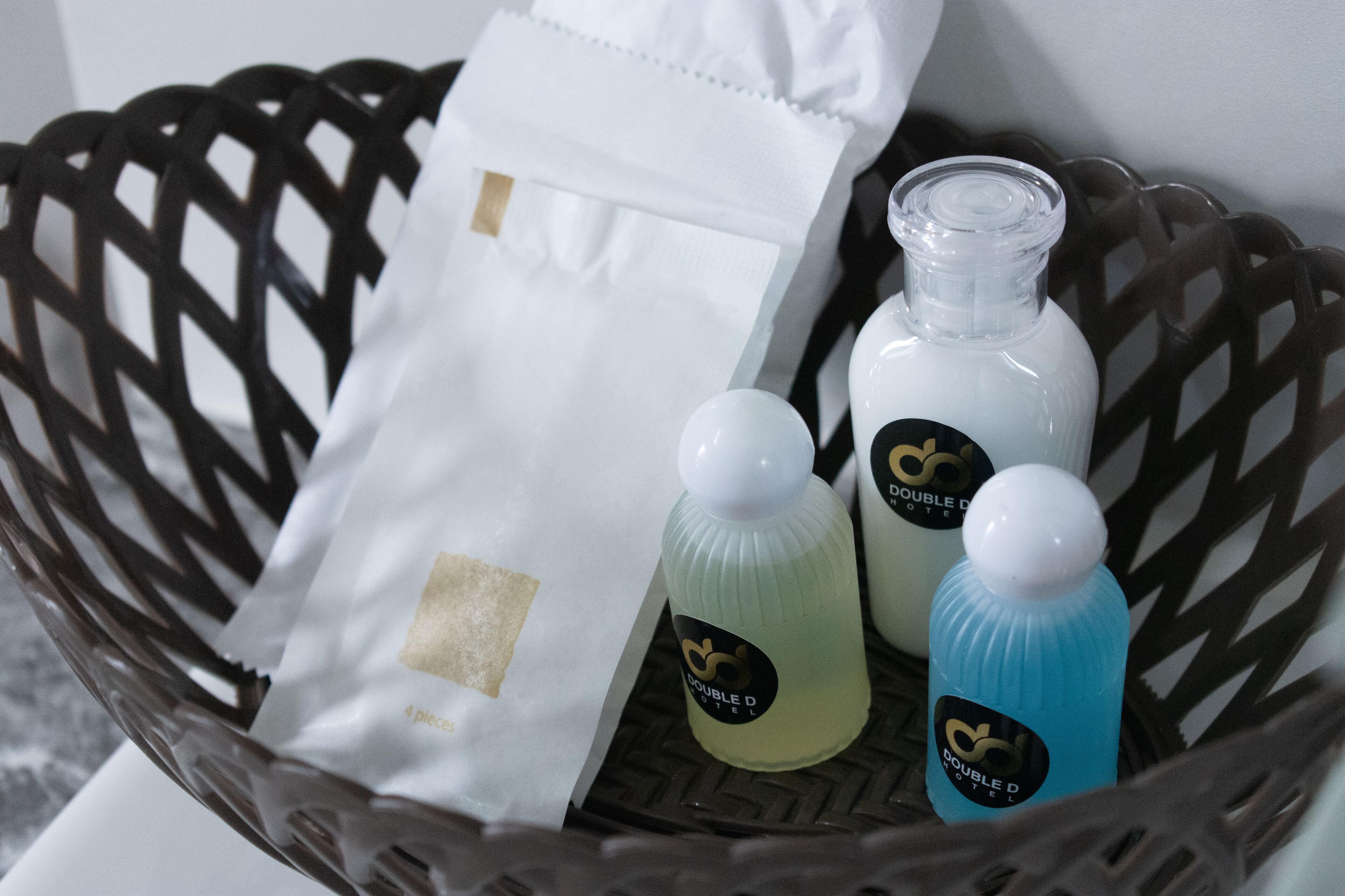 A wicker basket containing a white paper bag, two bottles with labels, and a clear bottle.