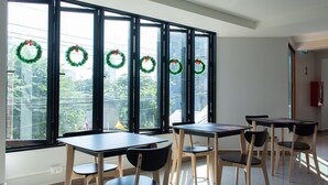 A room with large windows, multiple tables, and chairs arranged for dining. - Double D Hotel (Pak Kret)