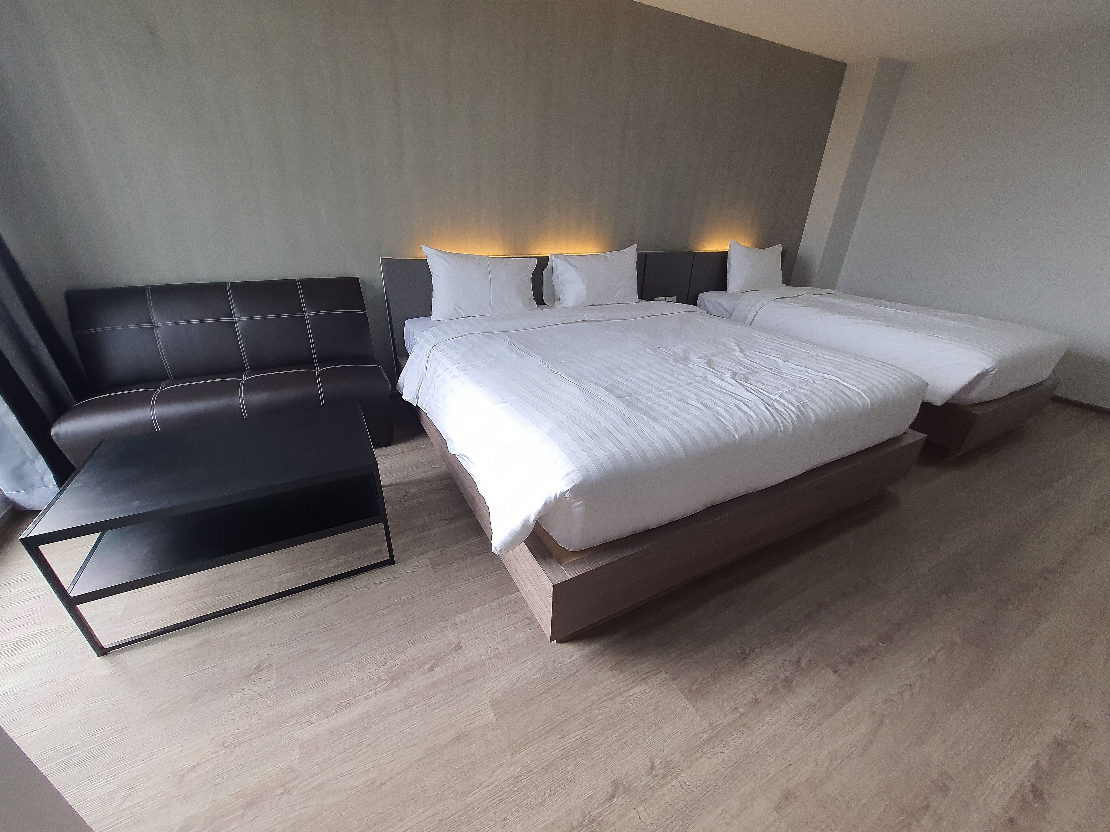 Una habitación de hotel moderna con una cama grande, un sofá de cuero negro y una mesita.