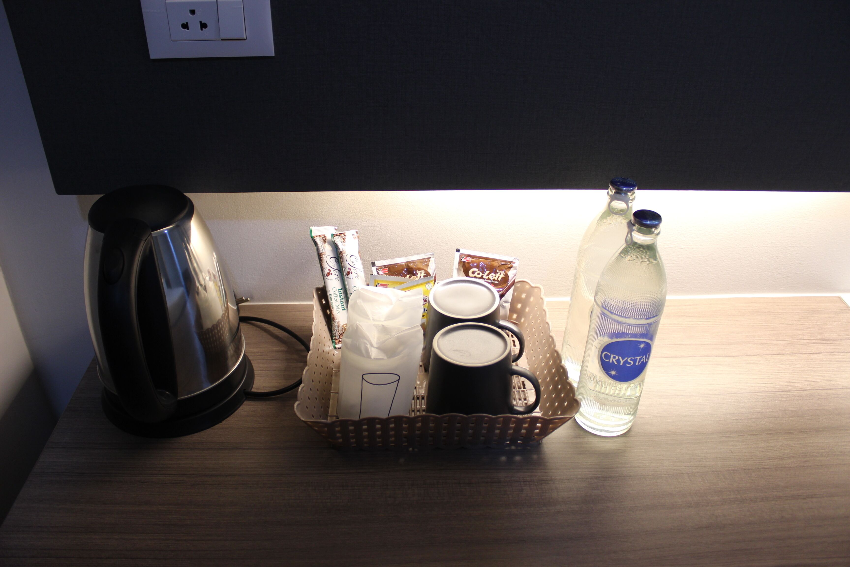 Una cafetera, una cesta con tazas de café, una botella de agua y un paquete de café sobre una mesa de madera.