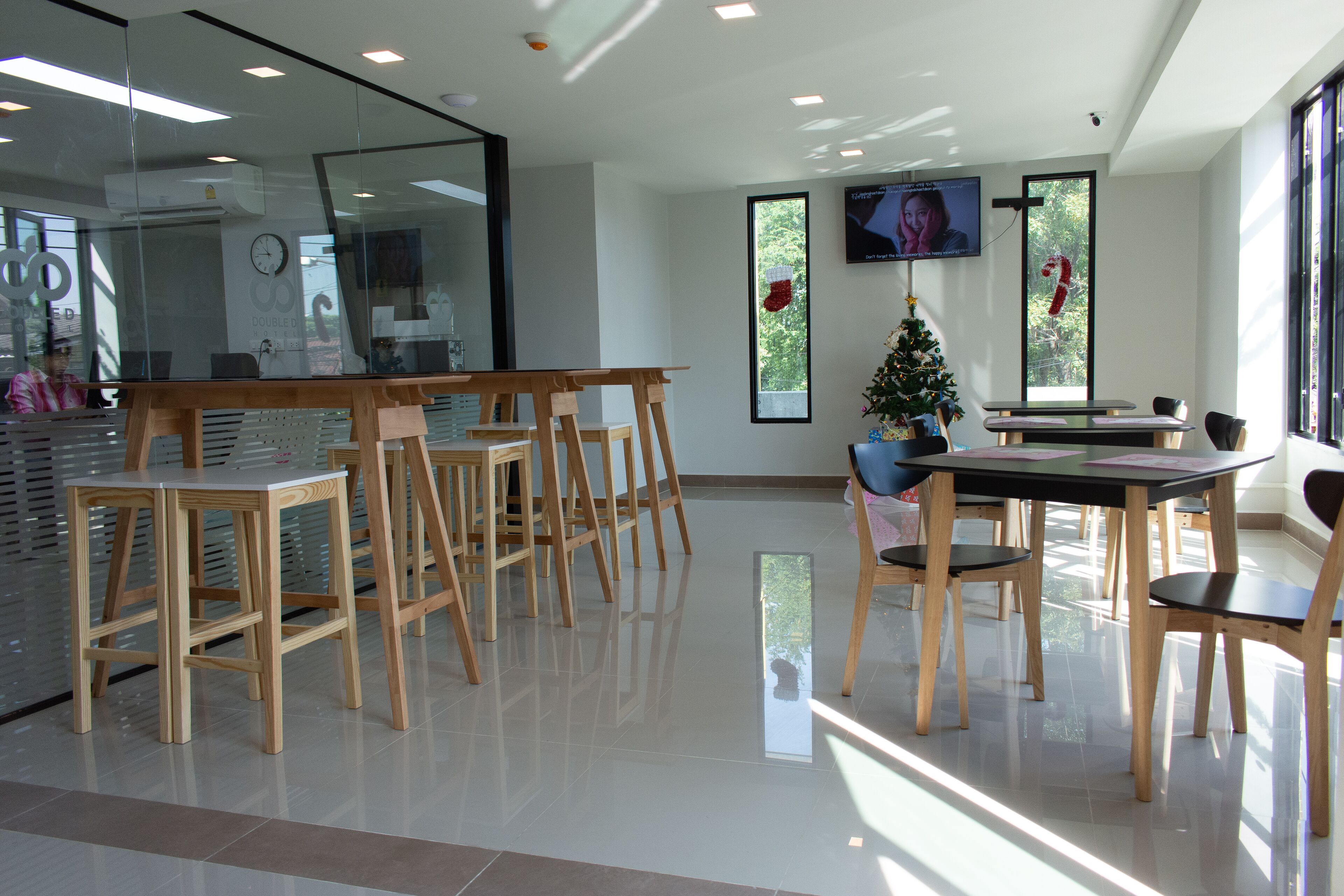 A modern interior with a glass wall, wooden chairs, a Christmas tree, and a TV on the wall.