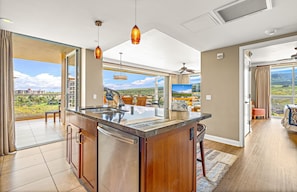 Une cuisine moderne dotée d’un grand îlot central, d’un coin repas offrant une vue agréable et d’un vaste espace de vie agrémenté d’un ventilateur de plafond.