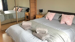 Ein Doppelbett mit gestreifter Bettwäsche und pinken, blumigen Kissen, ein Nachttisch aus Holz mit einer Lampe und ein hoher Kleiderschrank.