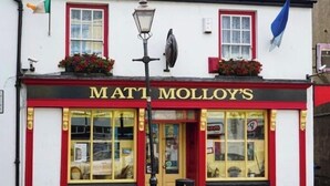 Eine Kneipe namens 'Matt Molloy's' mit einer rot-weißen Fassade, großen Fenstern und einem schwarzen Laternenpfahl davor.
