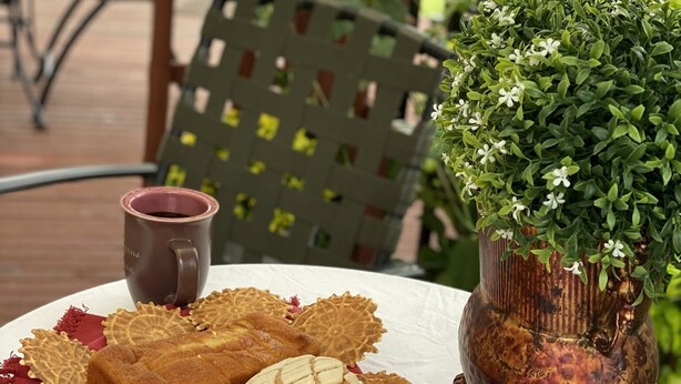 Una mesa con un plato de pasteles, una taza y una maceta decorativa.