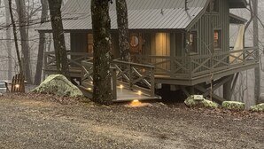 A rustic cabin with a wooden deck and a small porch, surrounded by trees.